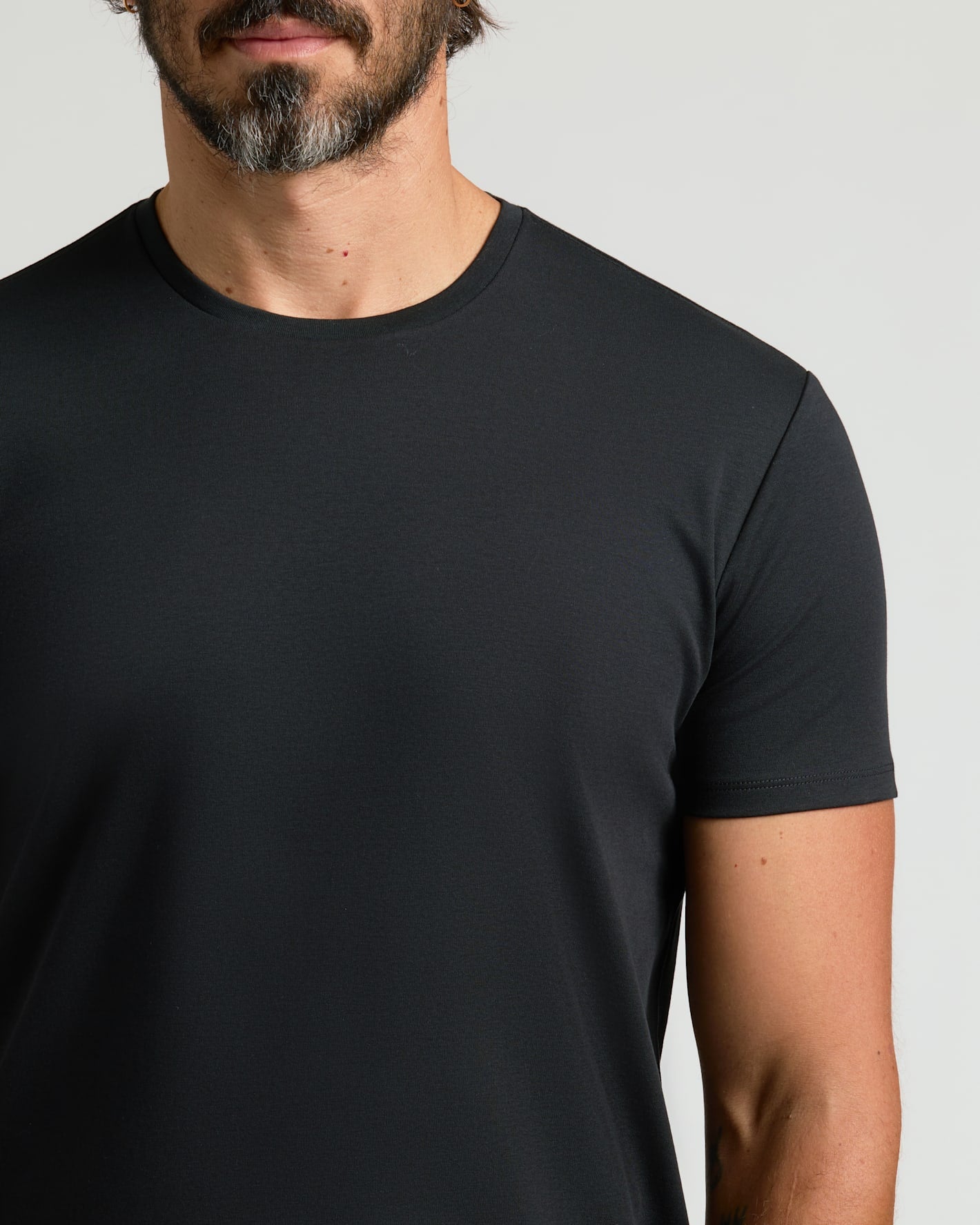 Close-up of a man wearing a black crew neck t-shirt, showcasing the smooth fabric and curved hem style of the Pima Cotton Blend Curved Hem Crew 7-Pack, a mens basics essential.