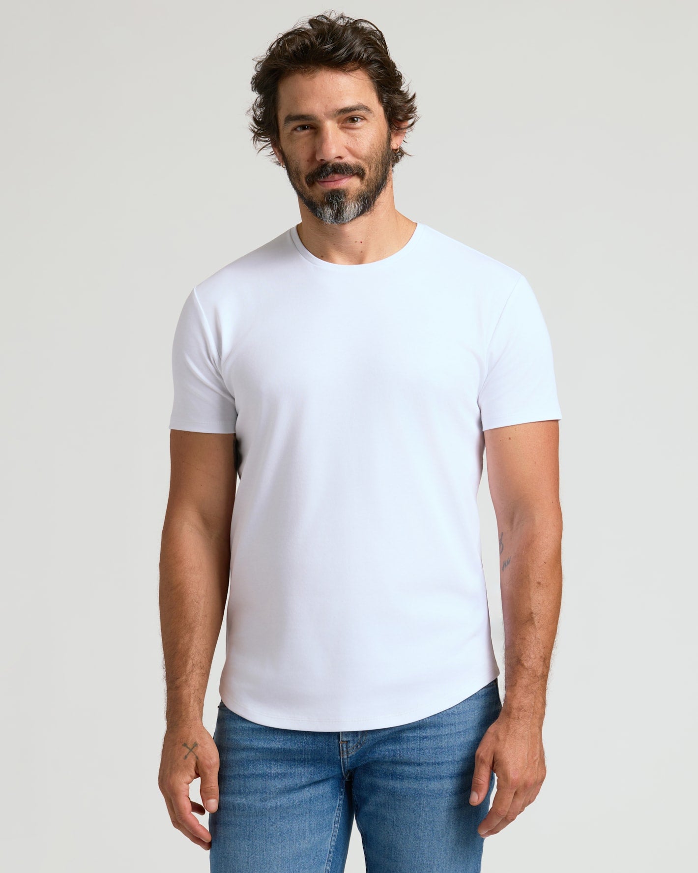 A man wearing a white Pima Cotton Blend Curved Hem Crew 7-Pack shirt paired with blue jeans, showcasing a clean and comfortable men's basics look.