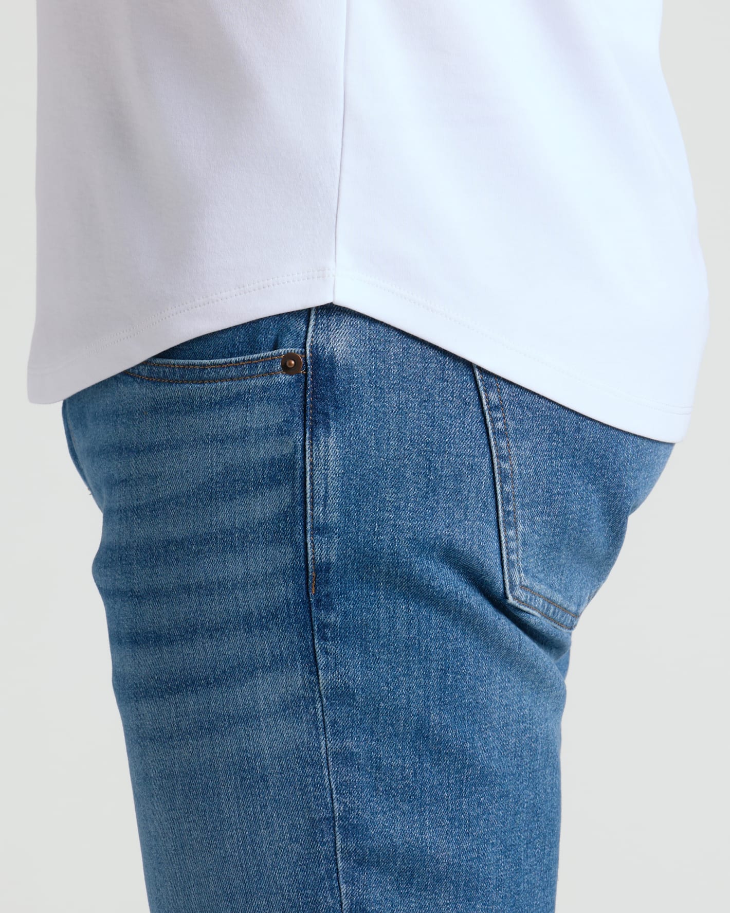 Detail close-up of a white Pima Cotton Blend Curved Hem Crew 7-Pack shirt worn untucked over blue jeans, highlighting the curved hem design and fabric texture.