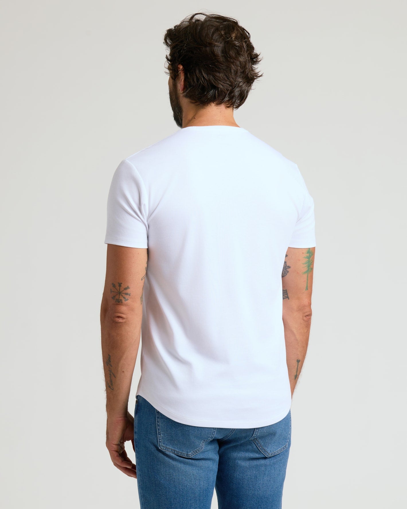 Man seen from behind wearing a white Pima Cotton Blend Curved Hem Crew 7-Pack t-shirt paired with blue jeans, showcasing a casual men's basics style.