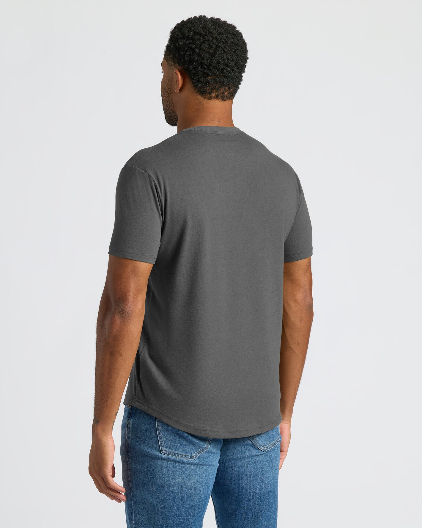Man wearing a gray t-shirt and blue jeans on a light gray background