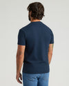 Man wearing a navy blue t-shirt and blue jeans on a light gray background