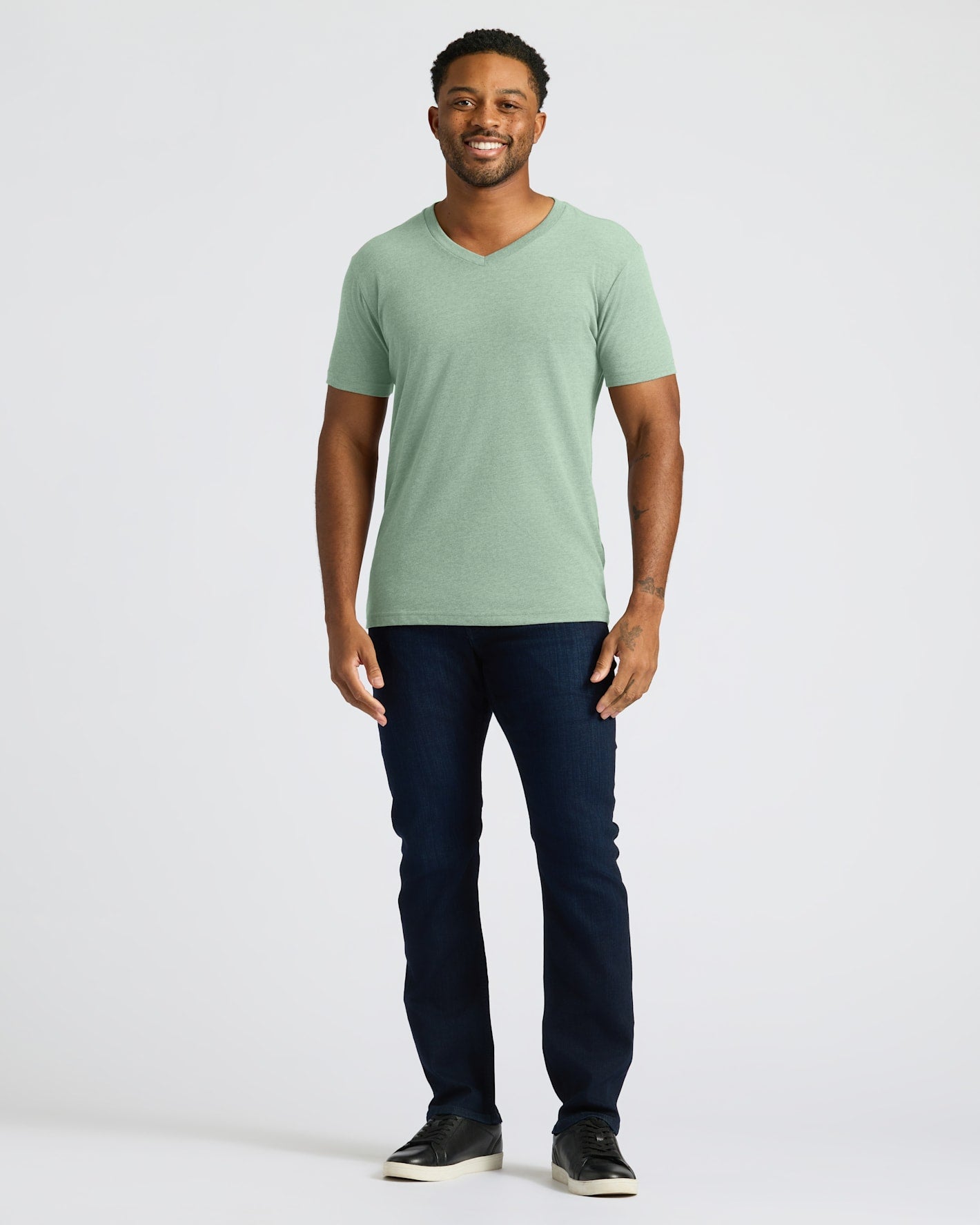 Man wearing a green t-shirt and dark jeans on a white background