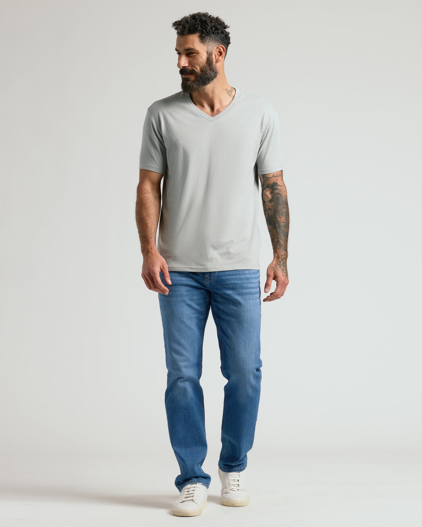 Man wearing Steel Classic V-Neck, blue jeans, and white sneakers.