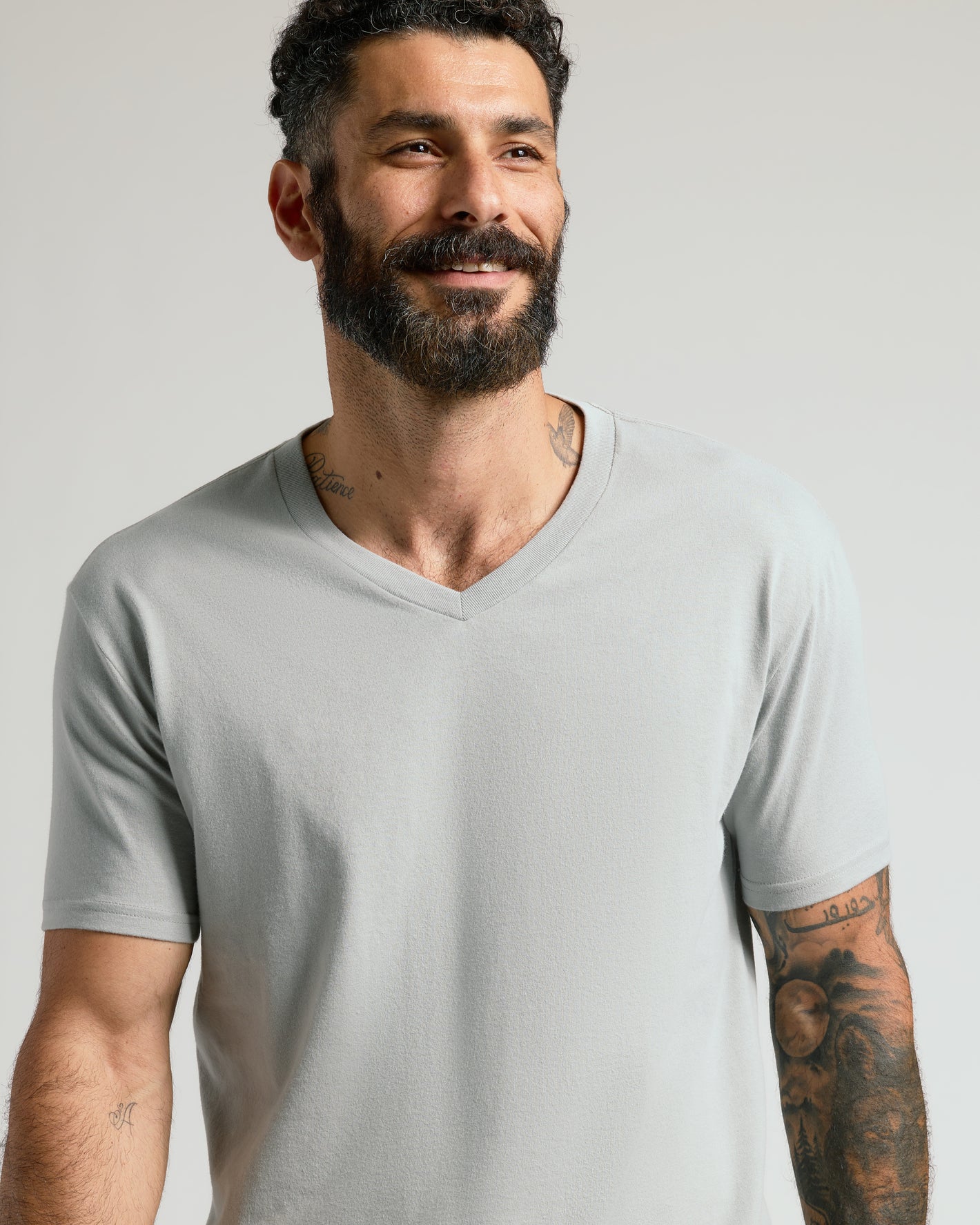 Smiling man in Steel Classic V-Neck, showcasing tattoos.