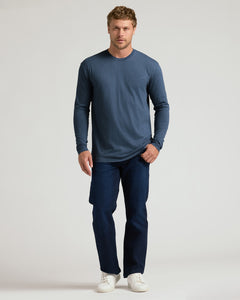 True ClassicA man modeling a slate blue long-sleeve crewneck shirt, dark blue jeans, and white sneakers against a light gray studio background.