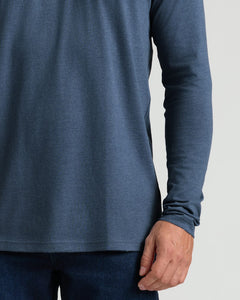 True ClassicClose-up of a person wearing a heathered slate blue long-sleeve shirt and dark blue jeans against a light gray background.