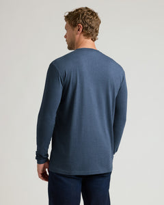 True ClassicA man viewed from the back wearing a heathered slate blue long-sleeve t-shirt and dark blue jeans, standing against a light gray studio background.