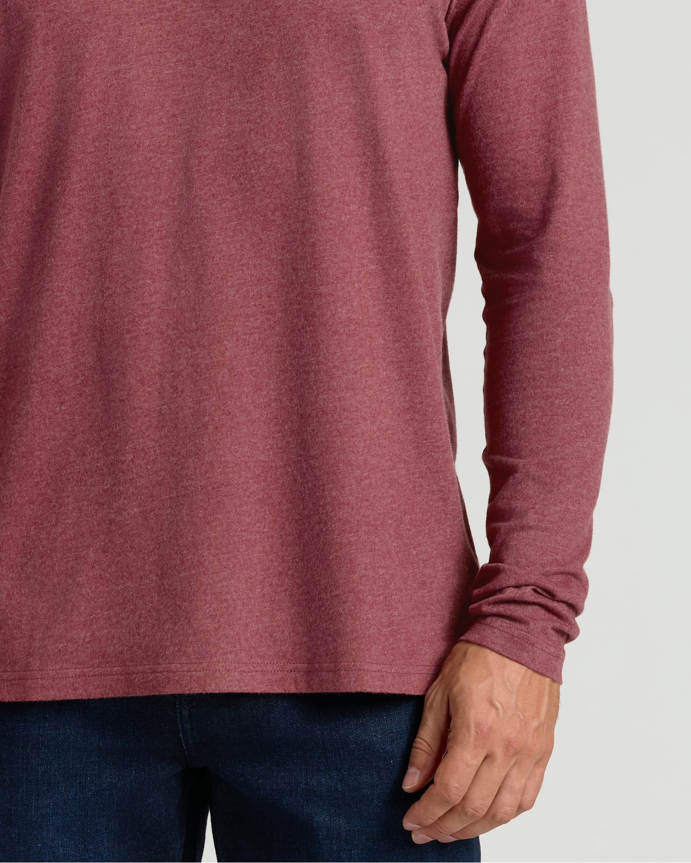 Close-up of a man wearing a Dark Heather Rustic Apple Classic Long Sleeve Crew Neck shirt in a soft, muted red tone paired with dark blue jeans, showcasing comfortable men's basics.