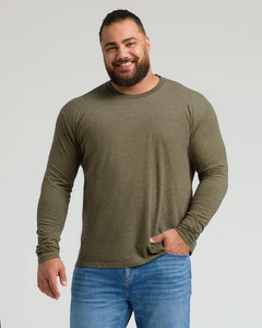 True ClassicA smiling man with a beard wearing an olive green long-sleeve crewneck shirt and blue jeans, standing against a light gray studio background.