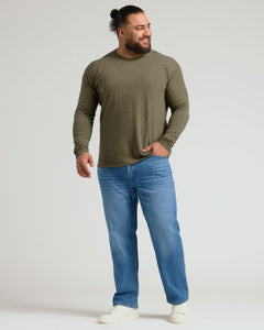 True ClassicA man wearing an olive green long-sleeve crewneck shirt, blue jeans, and white sneakers, standing against a light gray studio background.