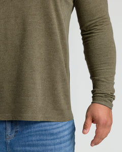 True ClassicClose-up of a person wearing a long-sleeve olive green shirt and blue jeans against a light gray background.