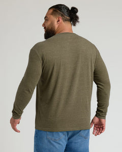 True ClassicA man with a beard and a bun, viewed from the back, wearing an olive green long-sleeve crewneck shirt and blue jeans against a light gray studio background.