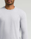 A close-up of a man wearing a light gray long-sleeve crewneck shirt against a plain light gray background.