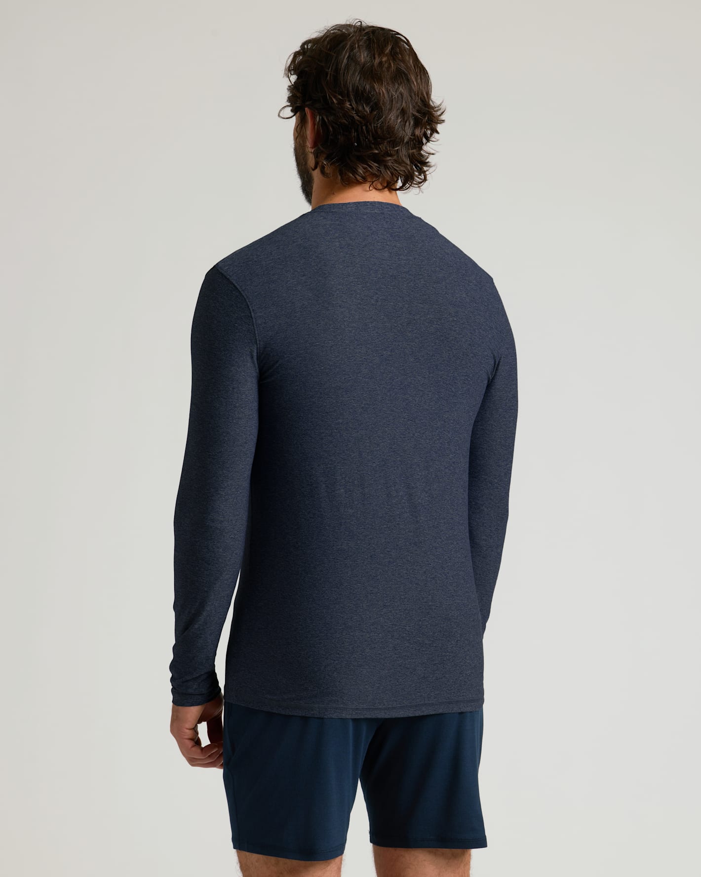 Man wearing a Dark Heather Fiord Active Long Sleeve Crew T-Shirt shown from the back, paired with dark athletic shorts, against a plain light background.