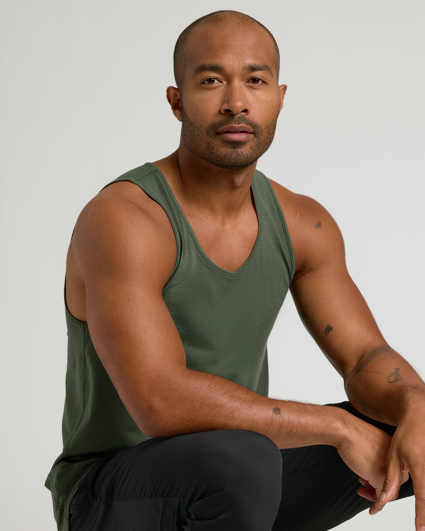 Man wearing Kelp Sleeveless Active Mesh Tank, crouched, showcasing athletic fit.