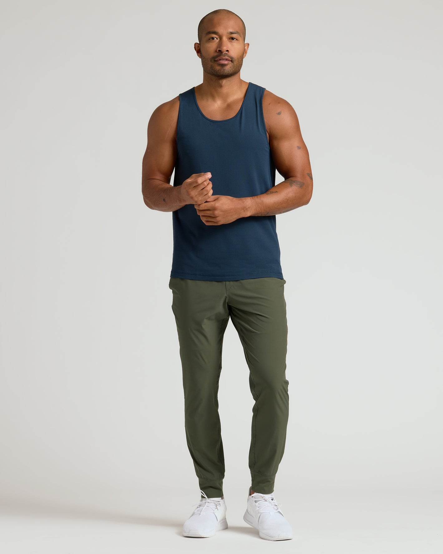 Man wearing Sleeveless Active Mesh Tank, navy, with olive joggers and white trainers.