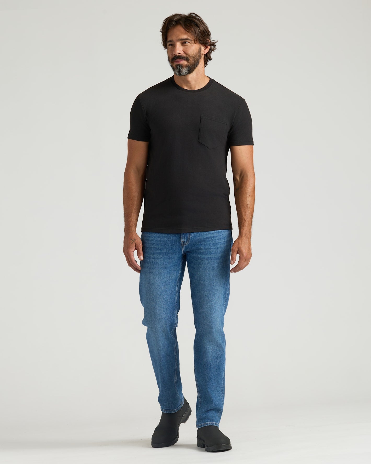Man wearing Black Heavyweight Pocket Crew, medium-wash jeans, black slip-on boots.