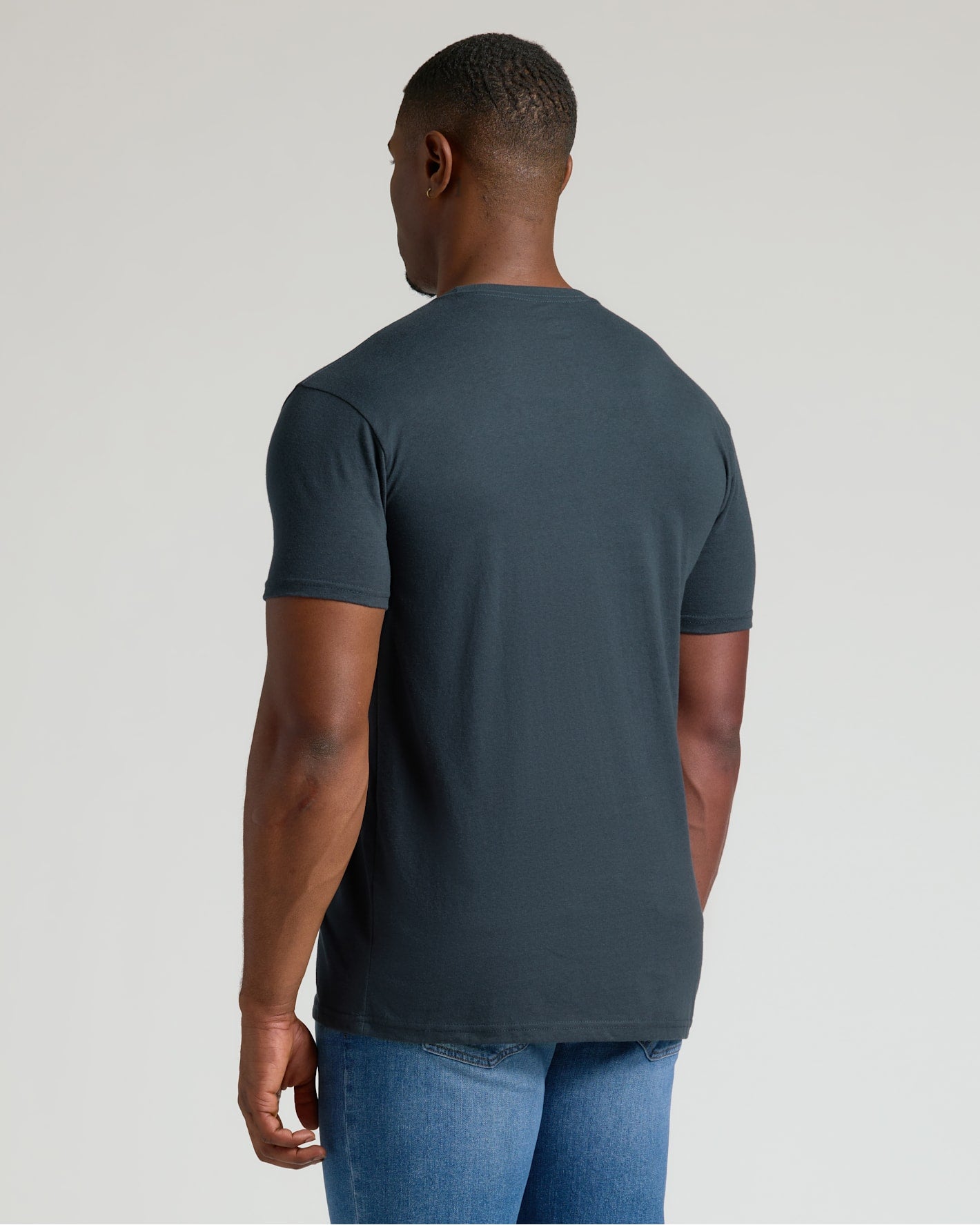 Man wearing a dark gray t-shirt and blue jeans on a light gray background