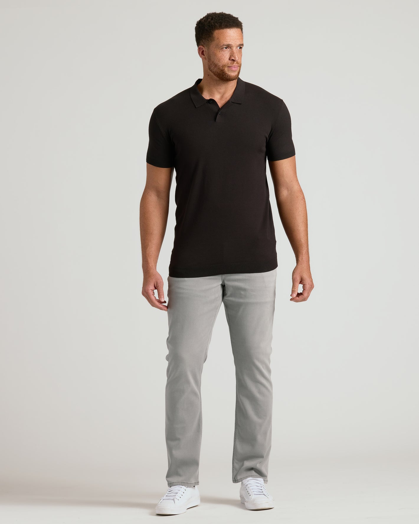 Man wearing Black Tall Dressy Polo with gray pants and white sneakers.