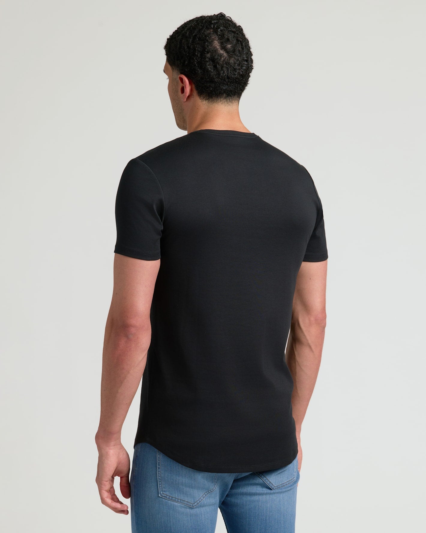 Man wearing a black Tall Pima Cotton Blend Curved Hem Crew 7-Pack t-shirt shown from the back, paired with light blue jeans against a plain background.