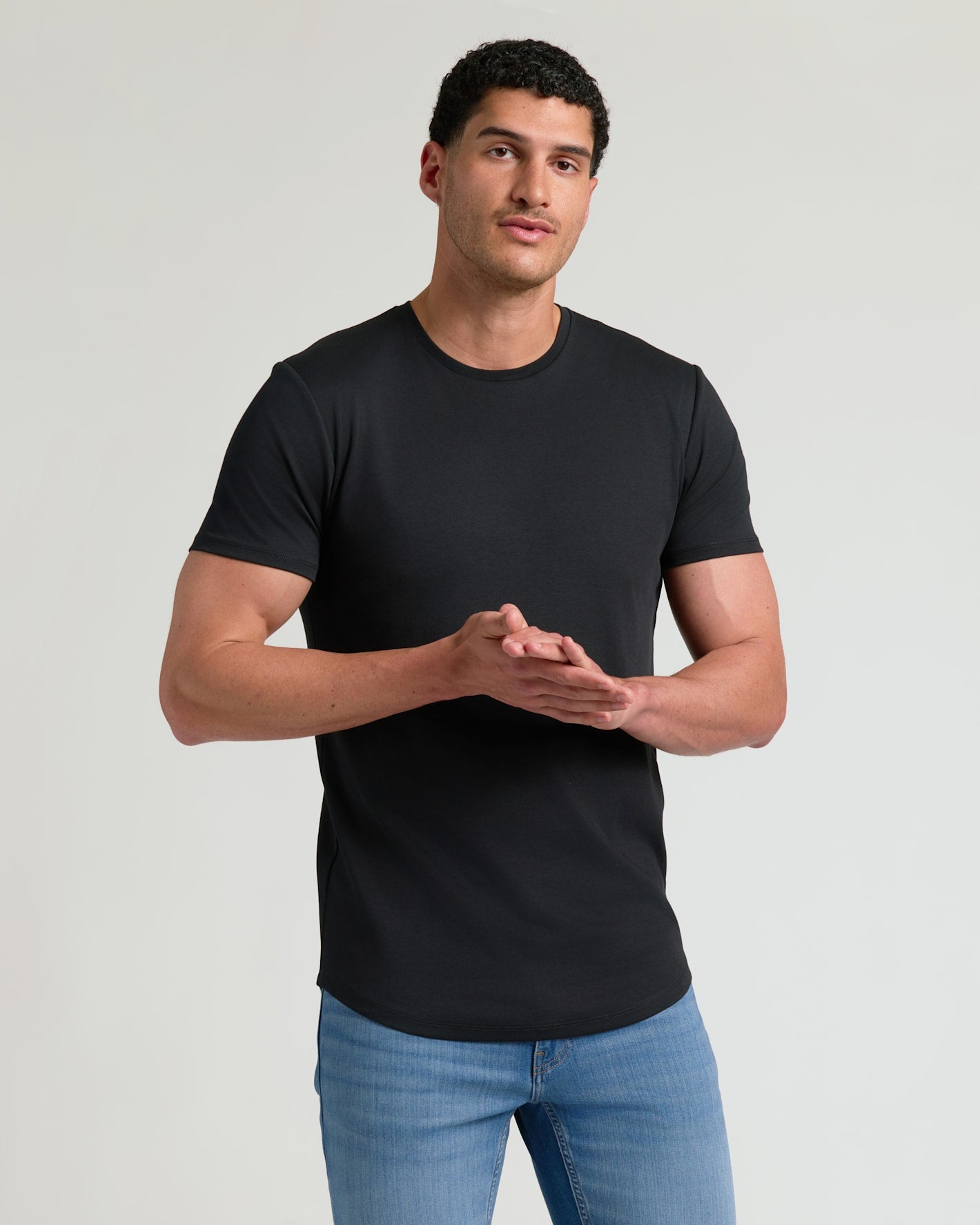 Man wearing a black Tall Pima Cotton Blend Curved Hem Crew 4-Pack t-shirt paired with blue jeans, showcasing a comfortable and fitted men's basics style.