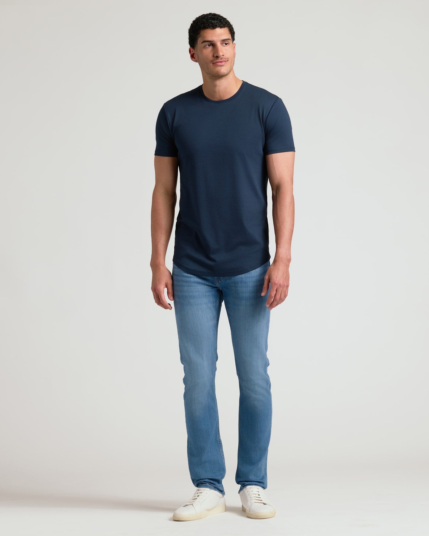 Man wearing a navy crew neck t-shirt with curved hem paired with light blue jeans and white sneakers, showcasing the Tall Pima Cotton Blend Curved Hem Crew 4-Pack in a casual style.