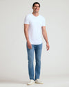 A smiling man wearing a white Tall Pima Cotton Blend Curved Hem Crew 4-Pack T-shirt paired with light blue jeans and white sneakers, standing against a plain background.