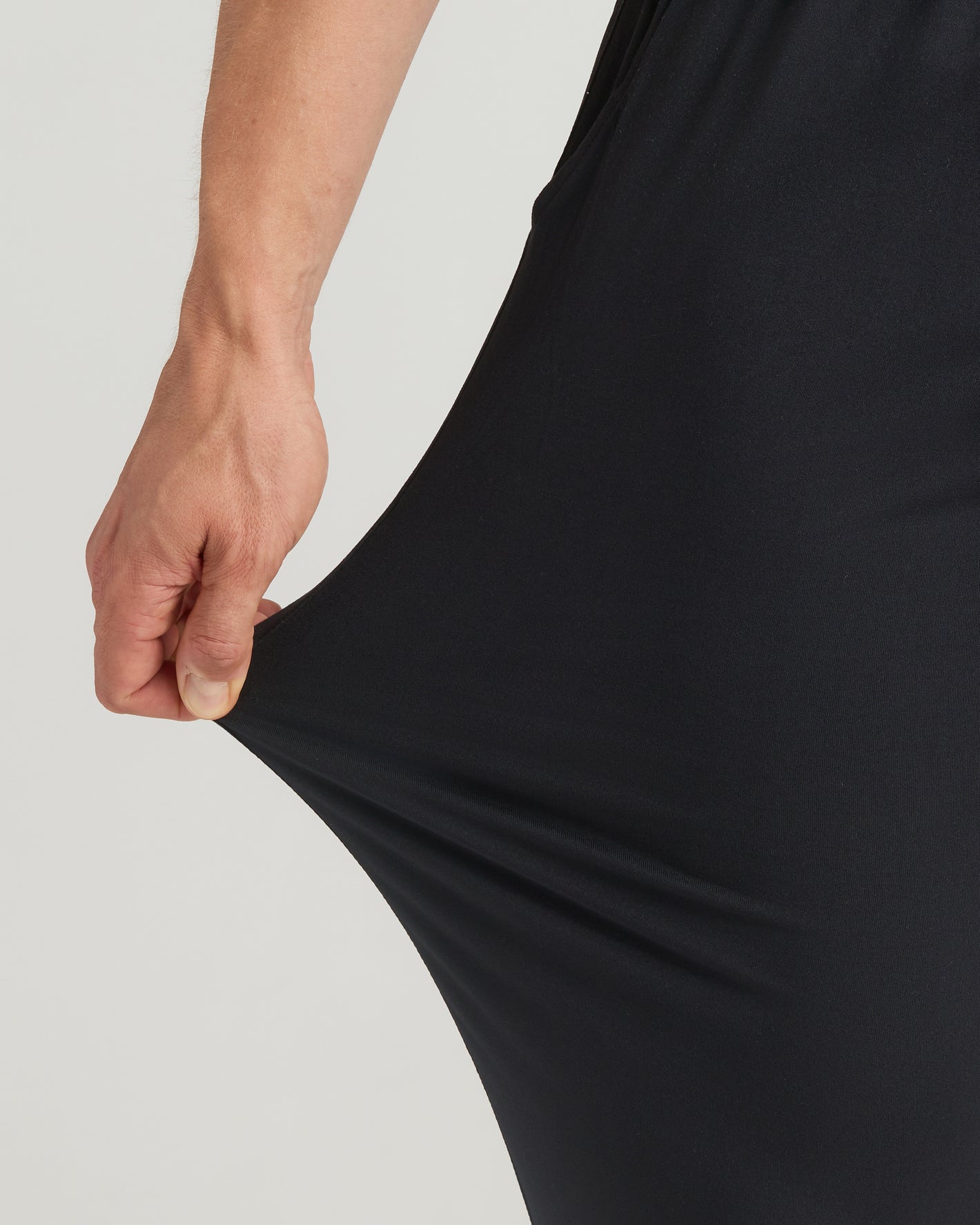 Hand stretching black fabric of Tall Active Joggers 3-Pack, showcasing flexibility.