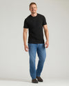Man wearing a black t-shirt and blue jeans on a light gray background