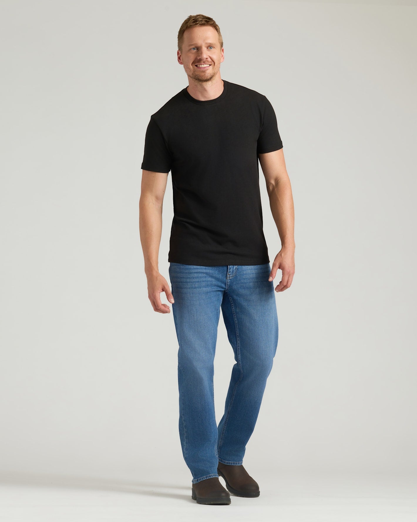 Man wearing a black t-shirt and blue jeans on a light gray background