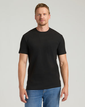 Man wearing a black t-shirt and blue jeans against a gray background