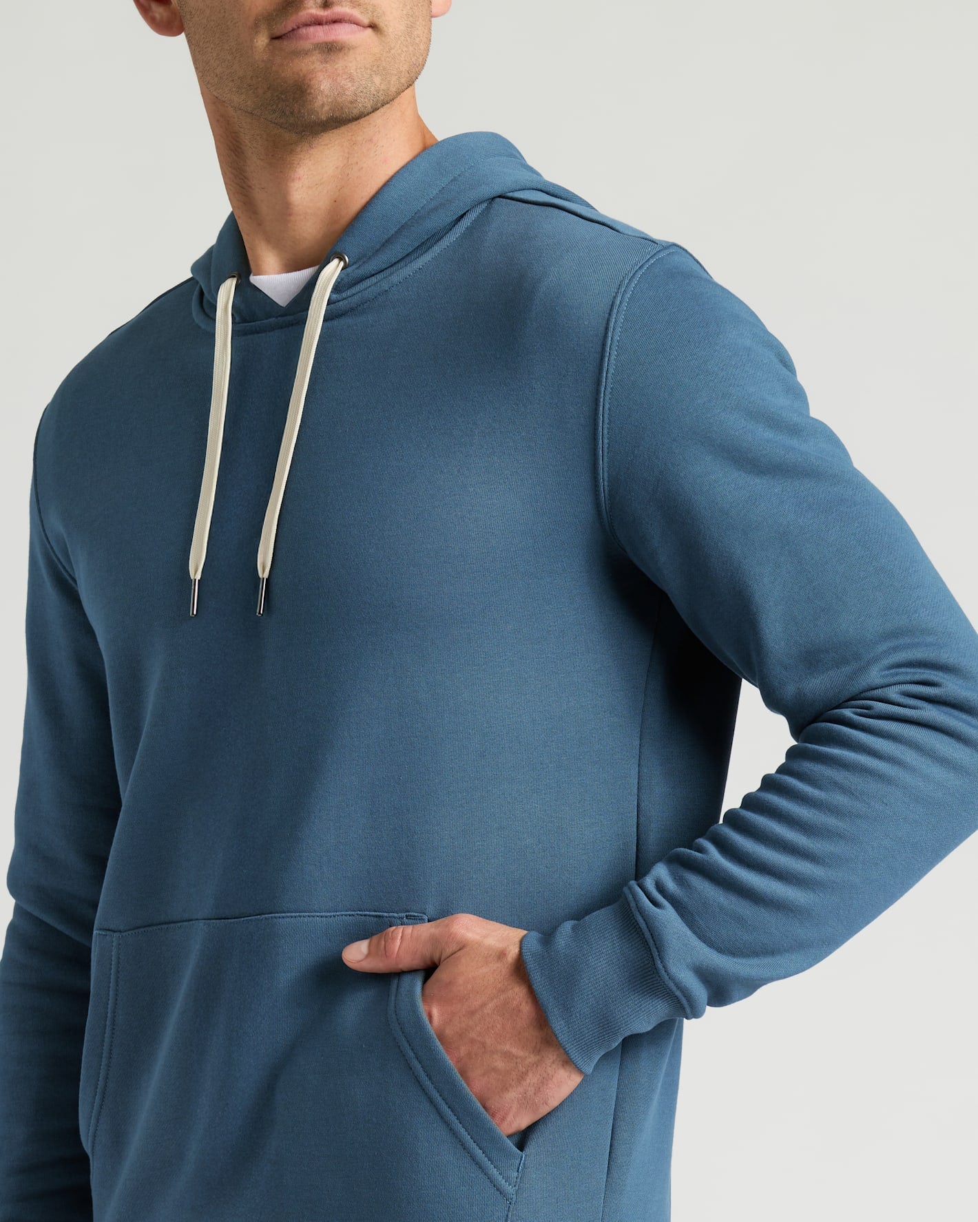 Man wearing a blue Fiord Fleece French Terry Pullover Hoodie with white drawstrings and a front pocket, showcasing comfortable men's basics in casual wear.