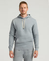 A man wearing a Dark Heather Gray Fleece French Terry Pullover Hoodie with a front kangaroo pocket and adjustable cream-colored drawstrings, styled as men's basics.