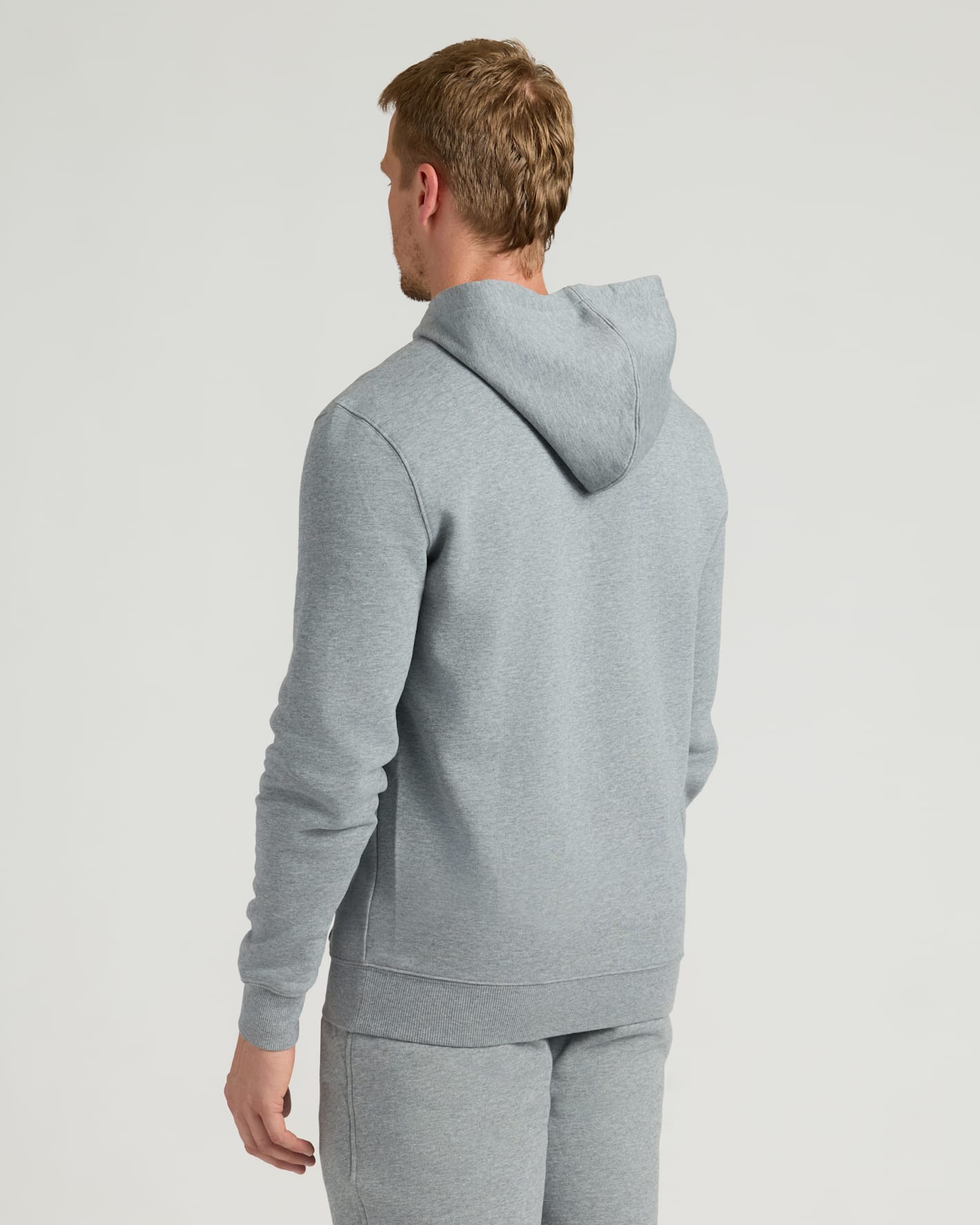Man wearing a Dark Heather Gray Fleece French Terry Pullover Hoodie viewed from the back, showcasing a comfortable fit and hood detail in a casual setting.