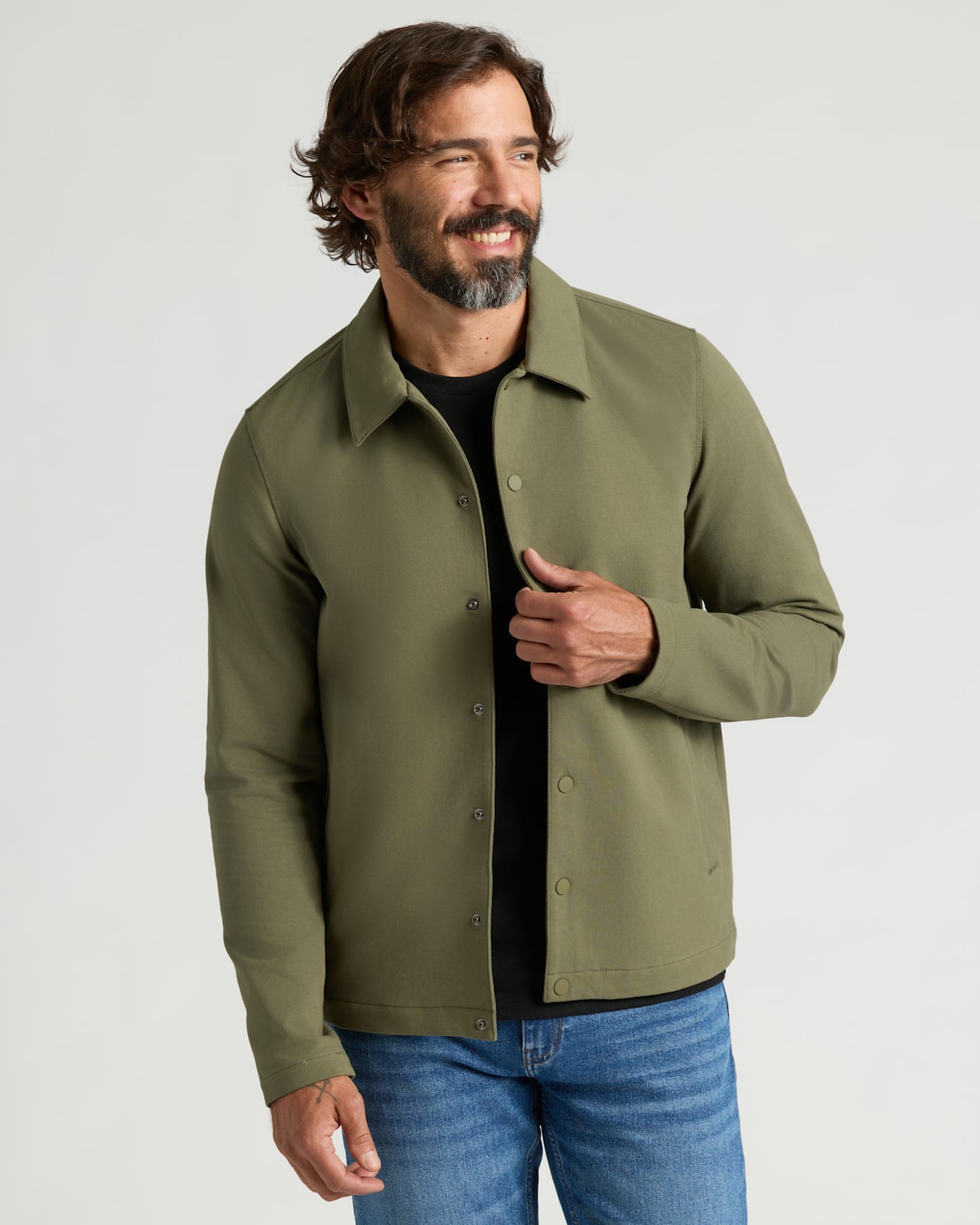 Man in Military Green Casual Jacket smiles, holding jacket front.