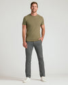 A man modeling a short-sleeve crewneck t-shirt in olive green and gray trousers, standing against a light gray studio background.