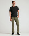 A man modeling a black short-sleeve crewneck t-shirt and olive green slim-fit trousers, paired with black sneakers, against a light gray studio background.