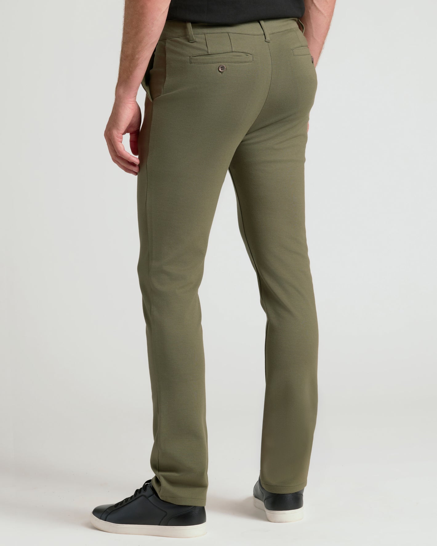 A man wearing olive green slim-fit trousers, shown from a rear three-quarter angle against a light gray studio background.