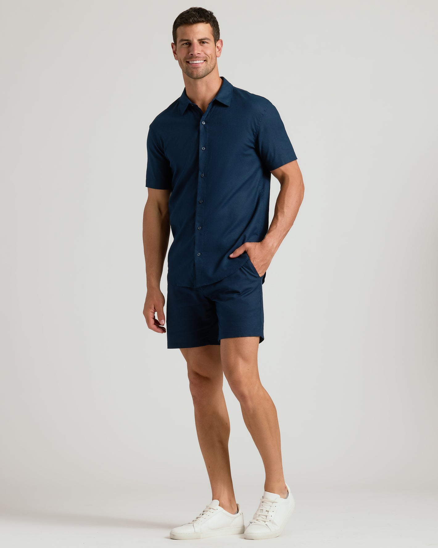 Man wearing 7 Navy Linen Shorts with a matching shirt and sneakers.