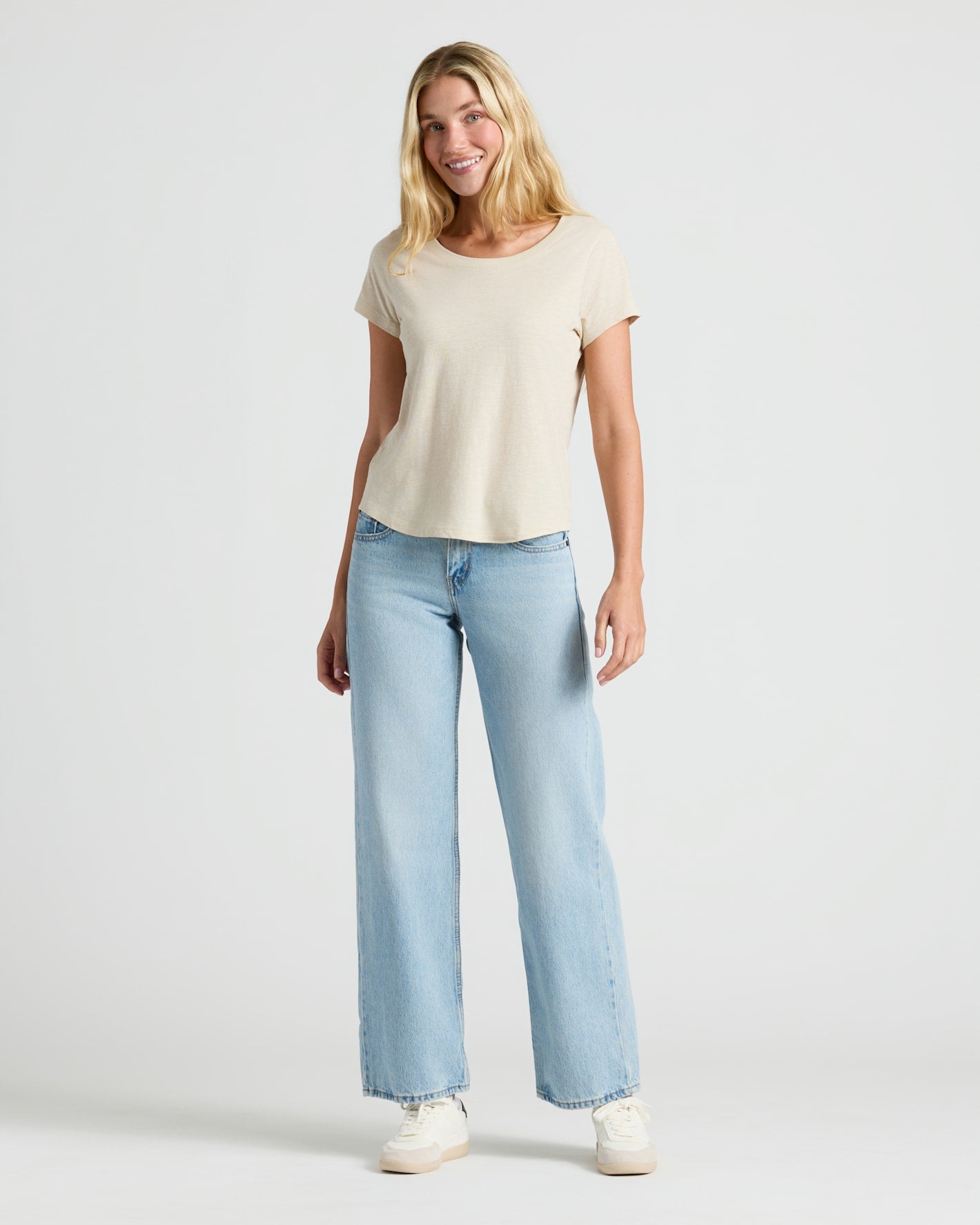 Woman wearing a beige t-shirt and light blue jeans on a white background