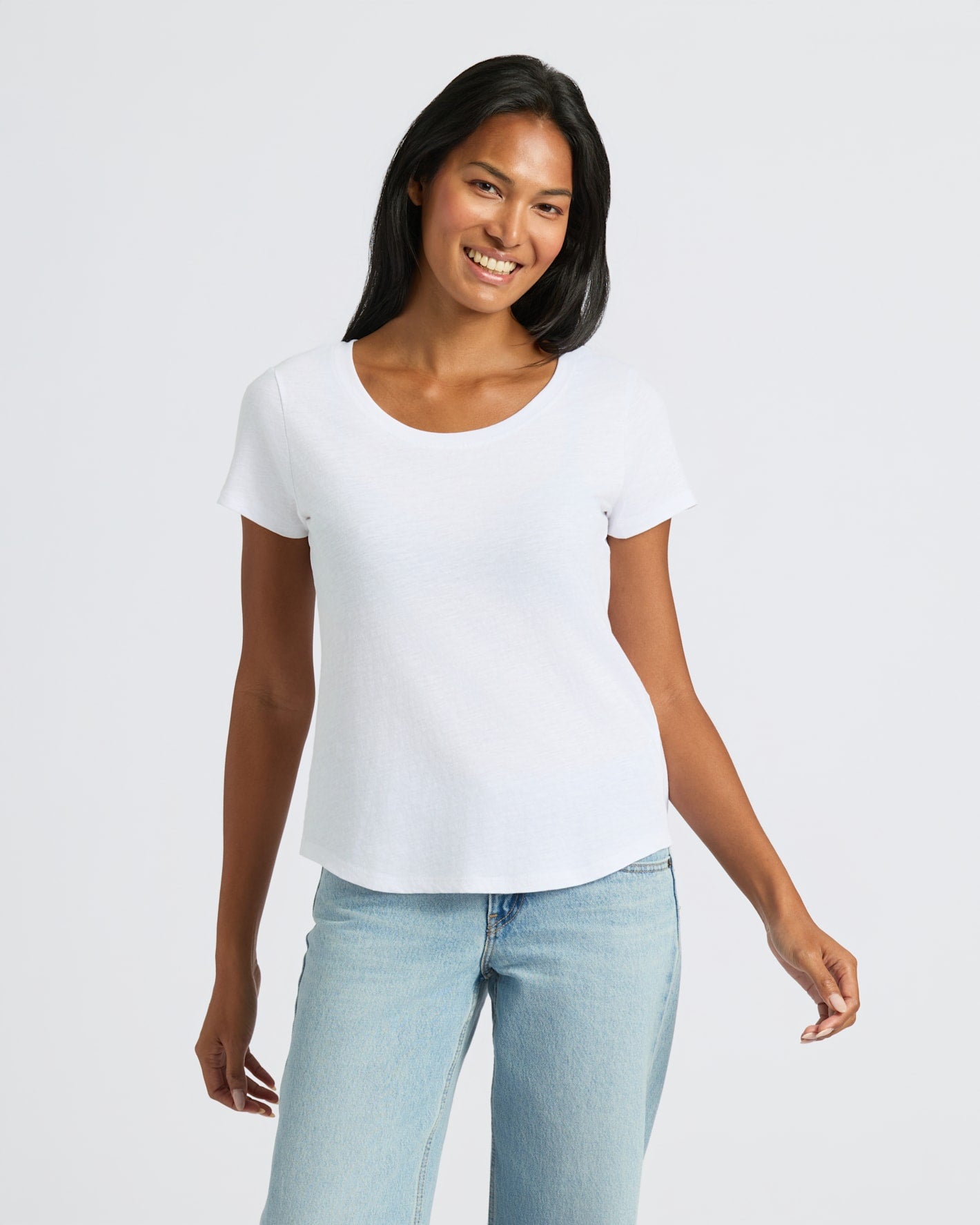 Woman wearing a white t-shirt and light blue jeans on a plain background
