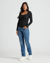 Woman wearing a black long-sleeve top and blue jeans on a white background