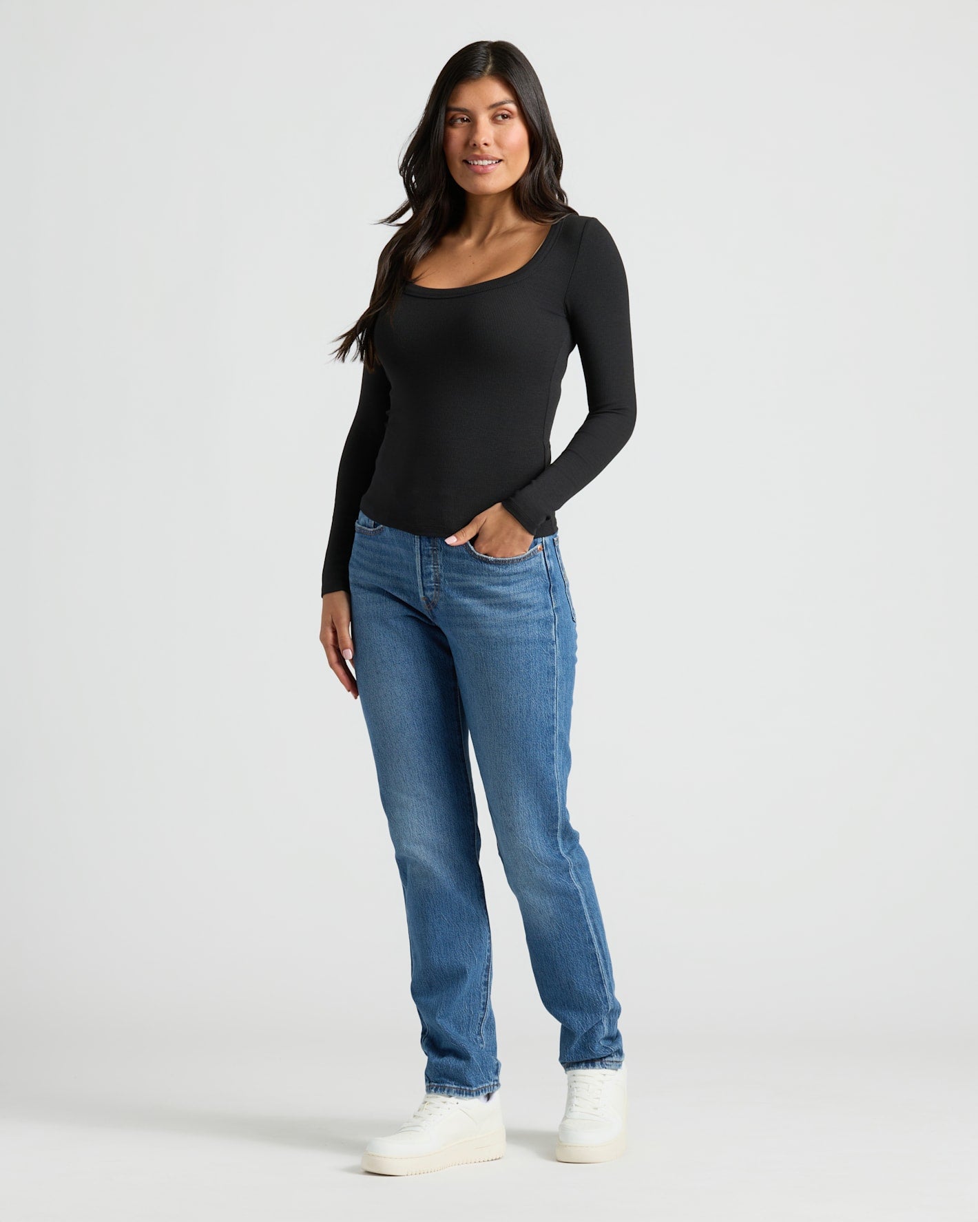 Woman wearing a black long-sleeve top and blue jeans on a white background