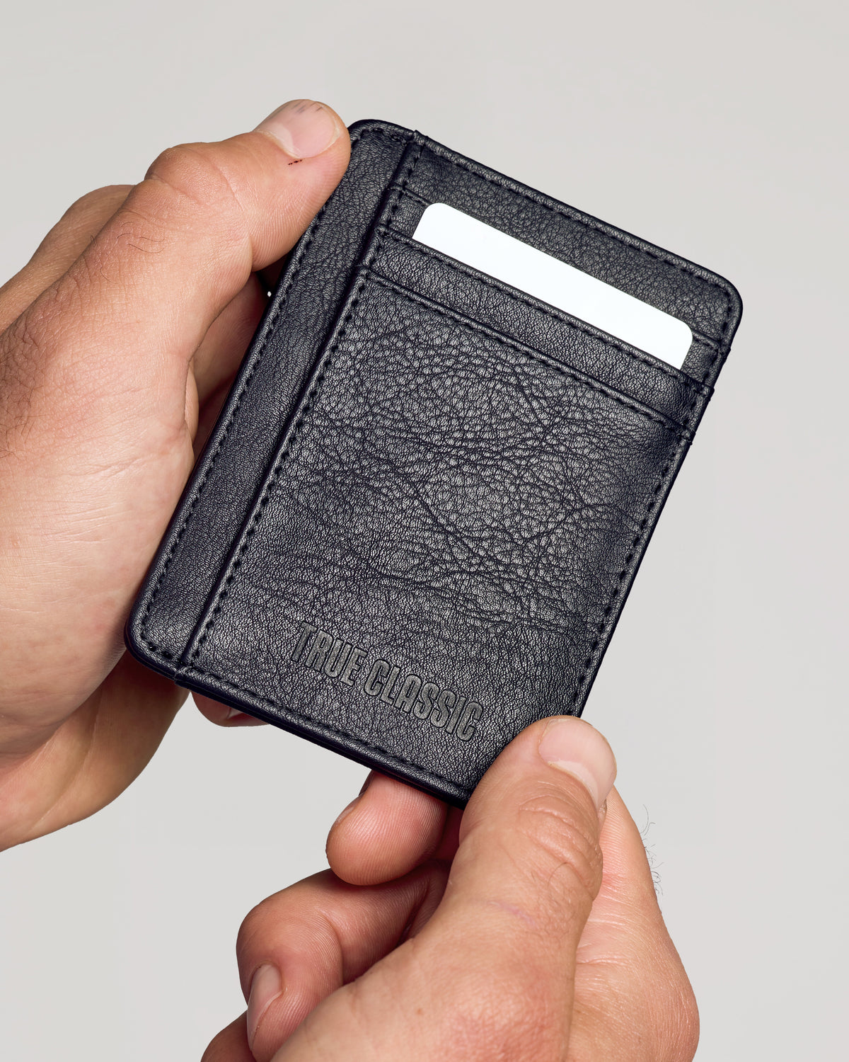 Black Classic Wallet held in hands, showcasing pebbled texture and TRUE CLASSIC embossing.