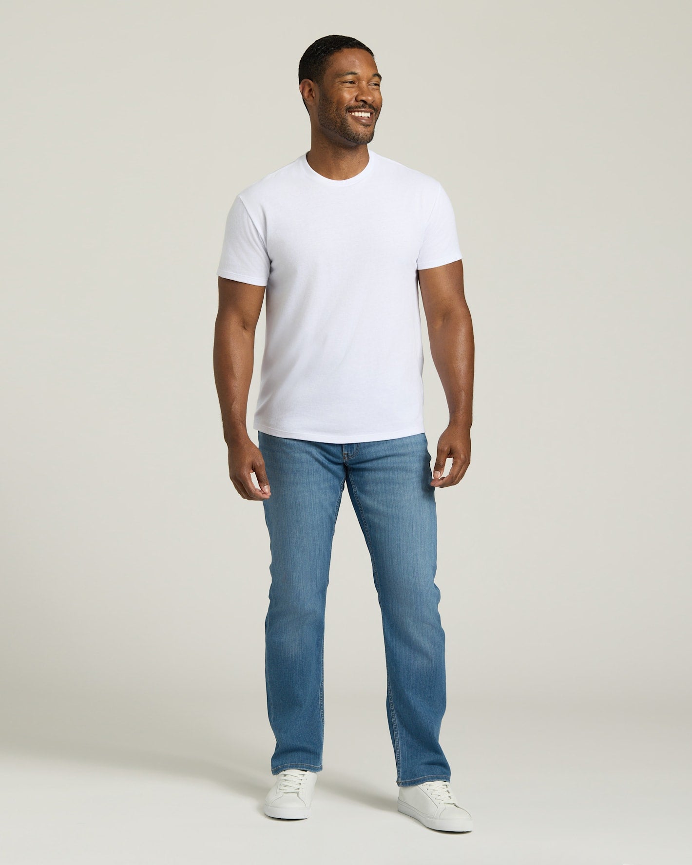 Man wearing a white t-shirt and blue jeans against a plain background. MODEL_INFO: Model is 5'8" wearing size M short