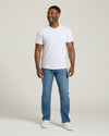 Man wearing a white t-shirt and blue jeans on a plain background. MODEL_INFO: Model is 5'8" wearing size M short