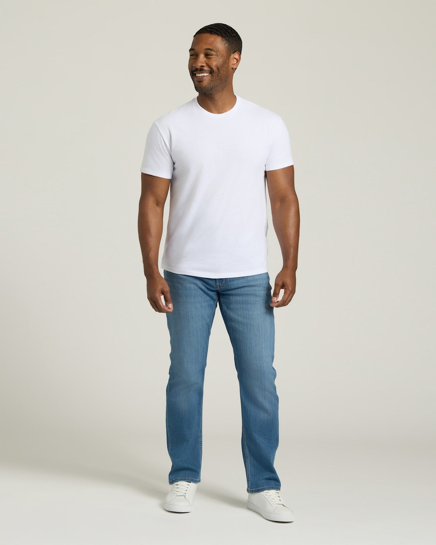 Man wearing a white t-shirt and blue jeans on a plain background. MODEL_INFO: Model is 5'8" wearing size M short