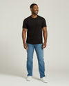 Man wearing a black t-shirt, blue jeans, and white sneakers on a plain background. MODEL_INFO: Model is 5'8" wearing size M short