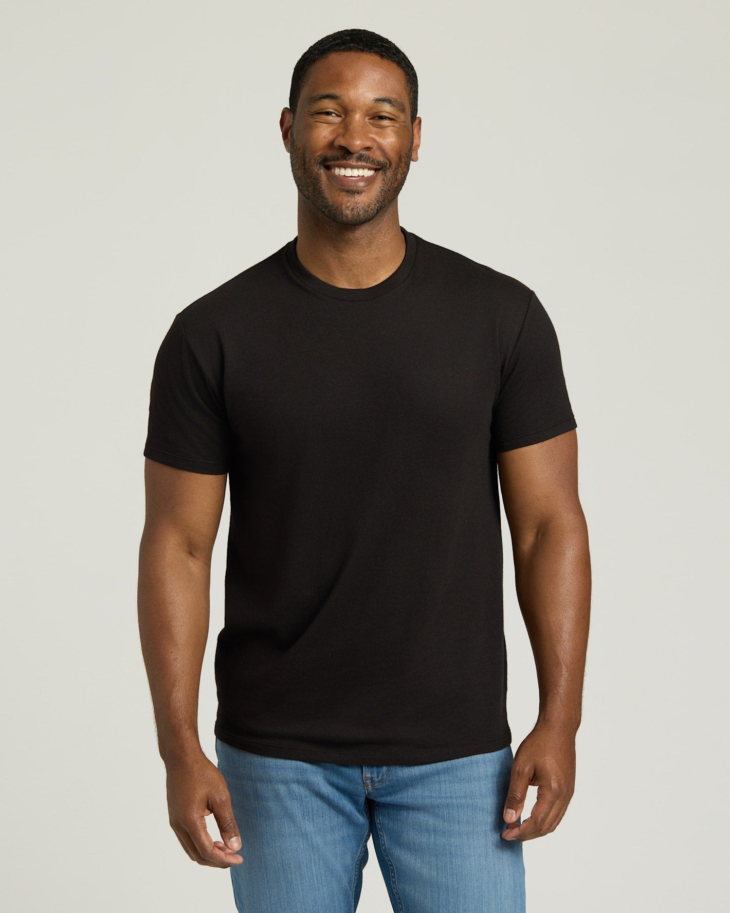 Man wearing a black t-shirt and blue jeans against a plain background